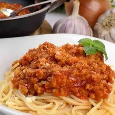 Spaghetti z sosem bolońskim, posypane parmezanem i udekorowane bazylią.
