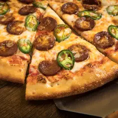 Kawałki pizzy z pepperoni i papryczkami jalapeño na drewnianym stole.